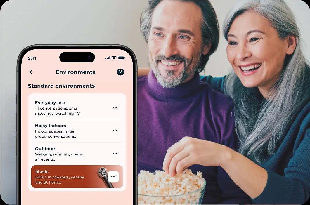 Man and woman eating popcorn and watching TV with Lexie hearing aids.