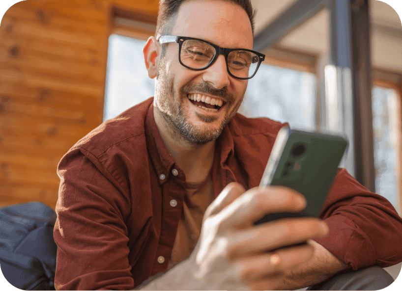 Man wearing glasses holding and smiling at his phone.